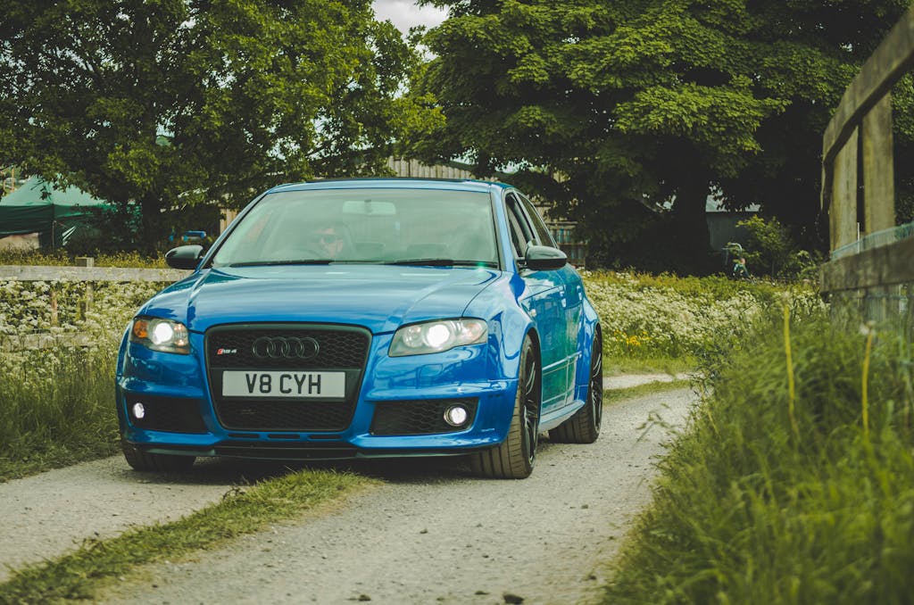 Modderguy A vibrant blue luxury car driving on a country road, framed by lush green surroundings.