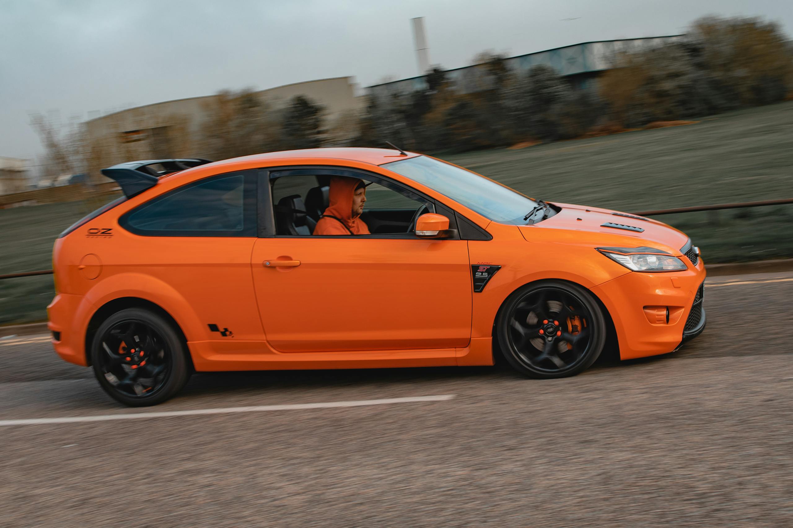 Modderguy An orange car driving swiftly on a road in Scotland, showcasing motion blur and focused energy.